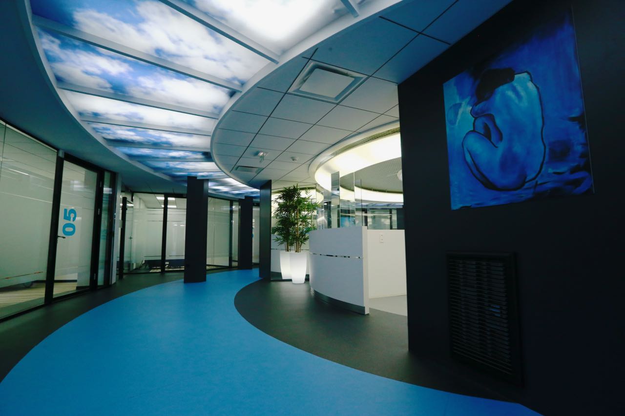 Couloir menant à un espace accueil circulaire à l’ambiance bleue, conçu par Arche du Bois — une transition fluide entre circulation et zone d’accueil au design immersif.