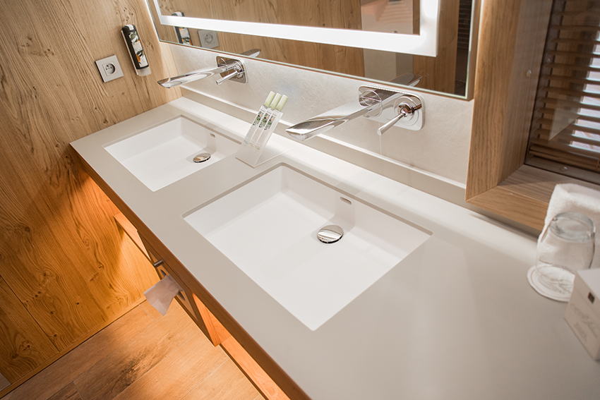 Deux lavabos avec robinets au design moderne, accompagnés d’un grand miroir rétroéclairé par LED, le tout intégré dans un décor mural en bois — un agencement élégant et fonctionnel signé Arche du Bois, combinant matériaux naturels et technologies lumineuses pour une salle d’eau sophistiquée.