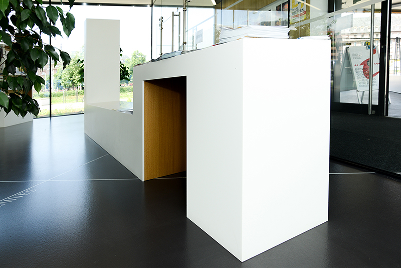 Table blanche posée sur un sol noir contrasté, avec un petit arbuste décoratif à gauche de l’image et une porte vitrée sur la droite