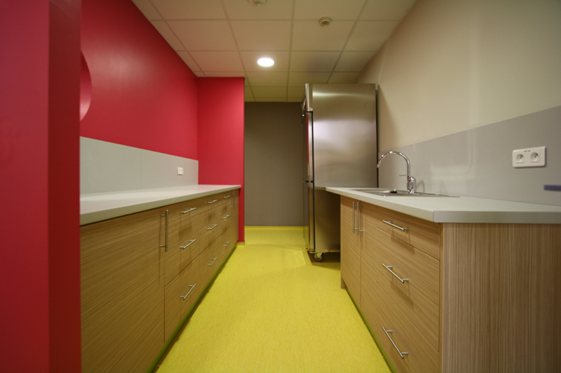 Couloir aménagé par Arche du Bois, avec un meuble en bois sur la droite contre un mur blanc, un grand rangement en bois sur la gauche contre un mur rouge, et un sol jaune apportant une touche chaleureuse à l’ensemble.