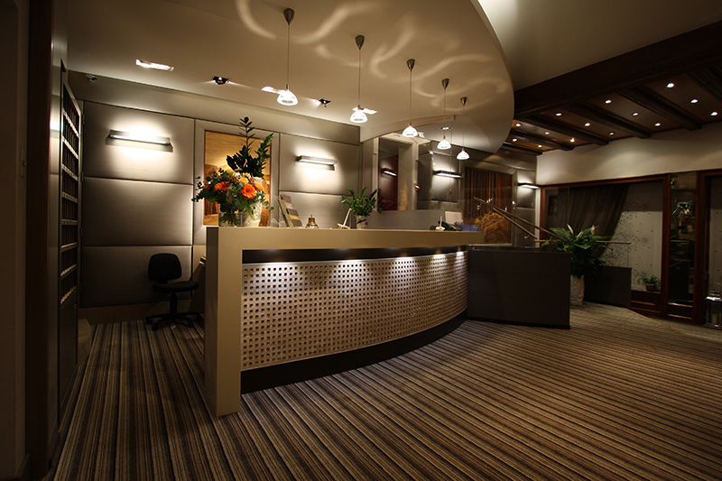 Comptoir arrondi de couleur marron, avec un éclairage intégré au-dessus et en dessous, conçu par Arche du Bois pour créer une atmosphère chaleureuse et accueillante dans l’espace d’accueil.