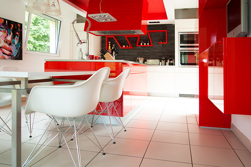 Vue d'une cuisine moderne avec un thème rouge et blanc. Sur la gauche de l’image, deux chaises sont placées autour d’une table, apportant un espace repas convivial et coloré