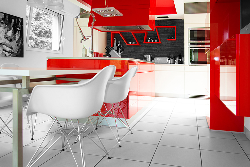 Vue d'une cuisine moderne avec un thème rouge et blanc. Sur la gauche de l’image, deux chaises sont placées autour d’une table, apportant un espace repas convivial et coloré.
