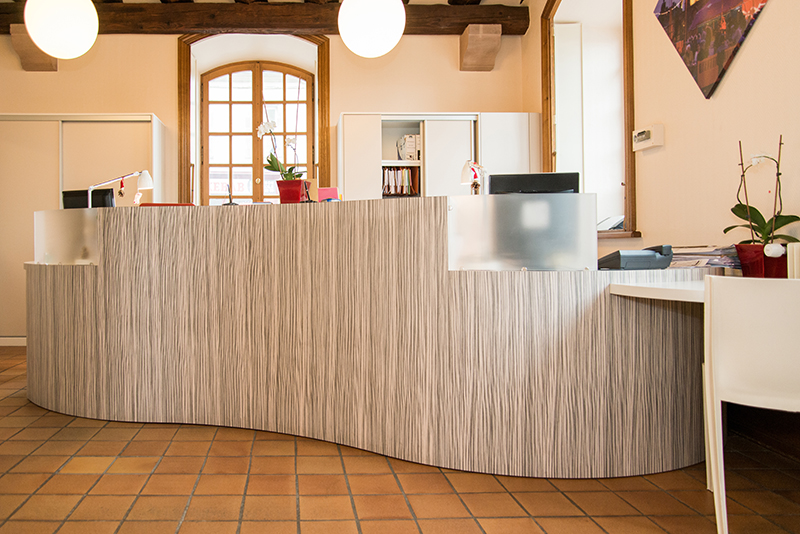 Comptoir d’accueil en bois courbé avec deux luminaires ronds suspendus au-dessus et une fenêtre à l’arrière