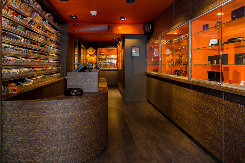 Comptoir en bois conçu par Arche du Bois, avec à l’arrière des étagères contenant des paquets de tabac, et sur la droite des boîtes de cigares soigneusement présentées — un agencement chaleureux et fonctionnel pour boutique spécialisée.