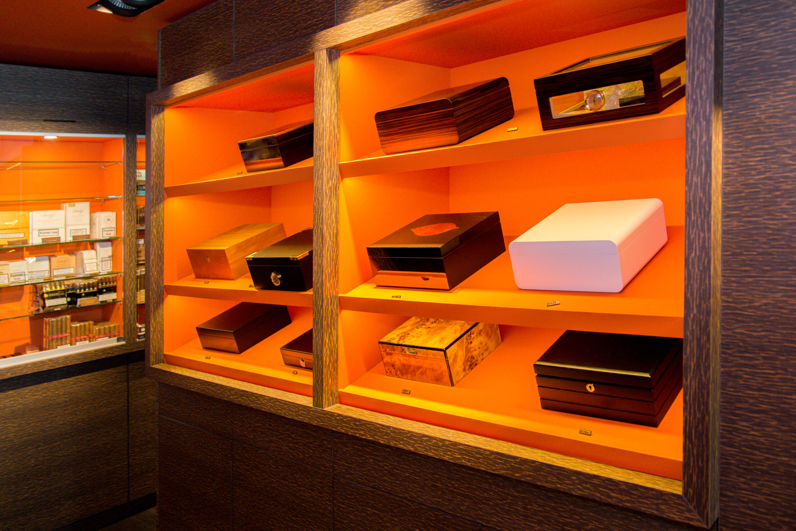 Étagères en bois avec structure extérieure naturelle et intérieur orange, contenant des paquets de cigarres soigneusement disposés — un agencement contrasté et sur mesure réalisé par Arche du Bois.