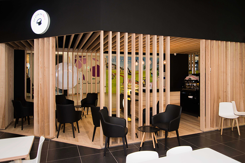 Salle de restauration Pizza de Nico avec des tables et chaises en noir et blanc, divisée en deux zones par des cloisons en bois — un agencement moderne et fonctionnel mettant en valeur l’identité graphique de l’enseigne dans un cadre structuré et chaleureux.