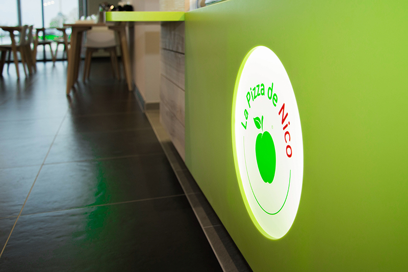 Logo lumineux et coloré de Pizza de Nico intégré à l’avant du comptoir d’accueil