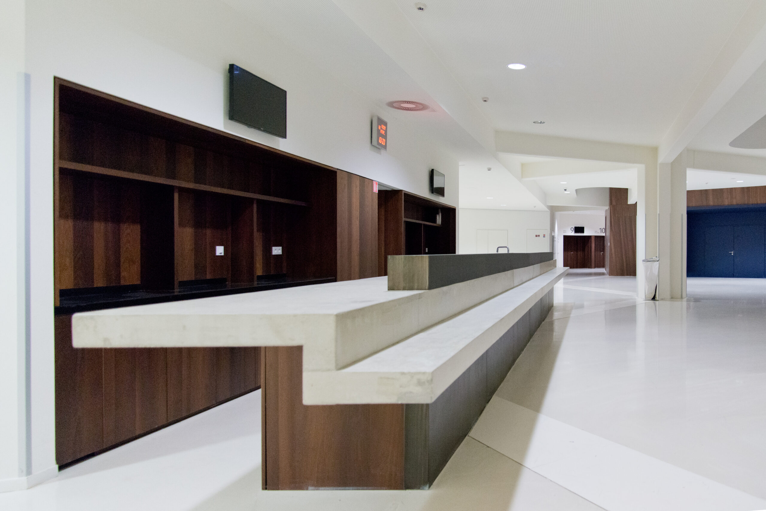 Comptoir d’accueil haut avec un soubassement en bois et un plateau supérieur blanc, accompagné à l’arrière d’une étagère murale en bois