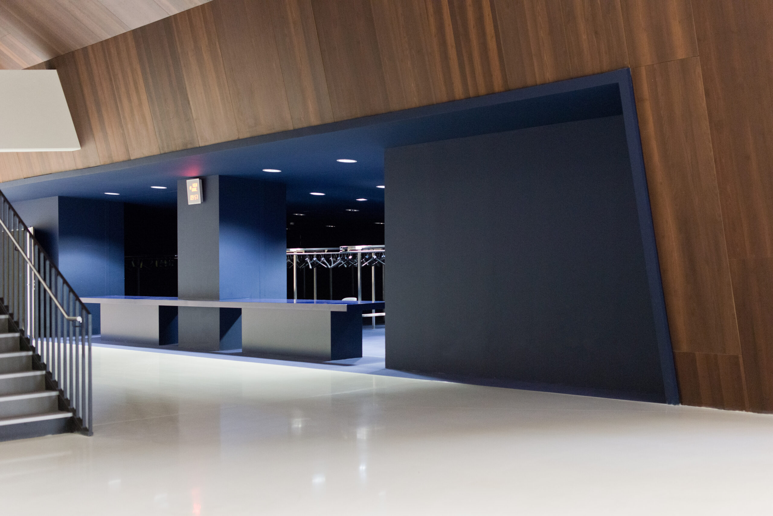 Grande entrée peinte en bleu, entourée de murs habillés de bois naturel, avec une partie d’un escalier visible sur la gauche