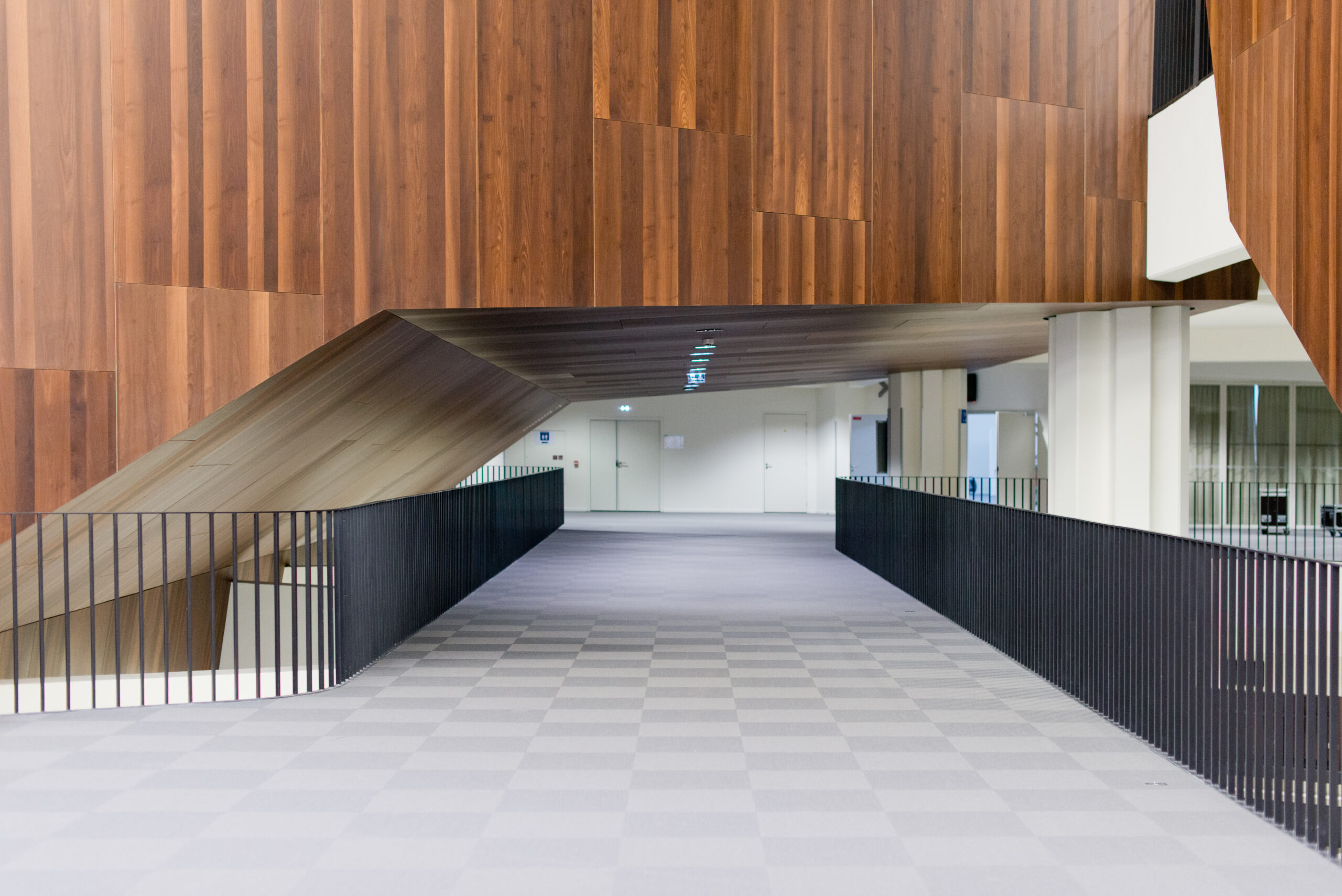 Couloir encadré de garde-corps de chaque côté, menant à un mur en bois naturel au fond