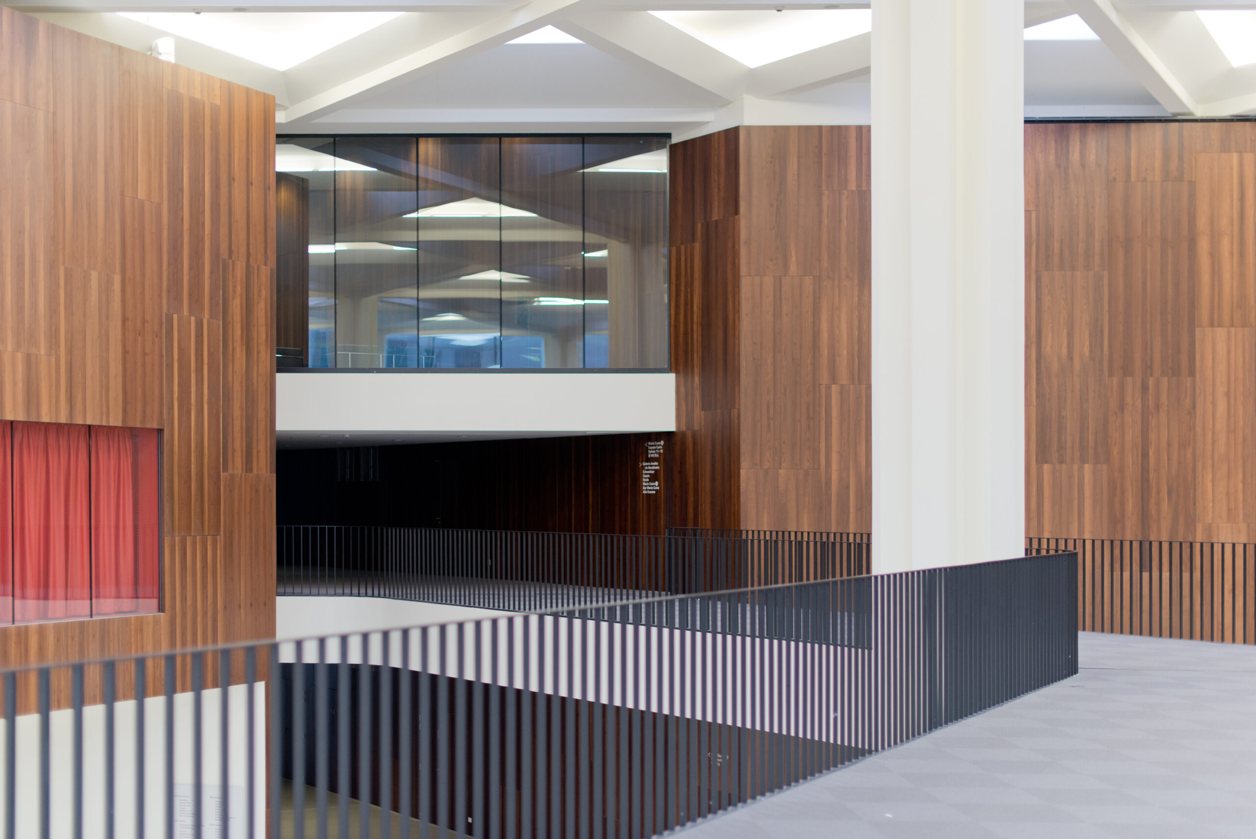 Couloir encadré de garde-corps de chaque côté, menant à un mur en bois naturel au fond