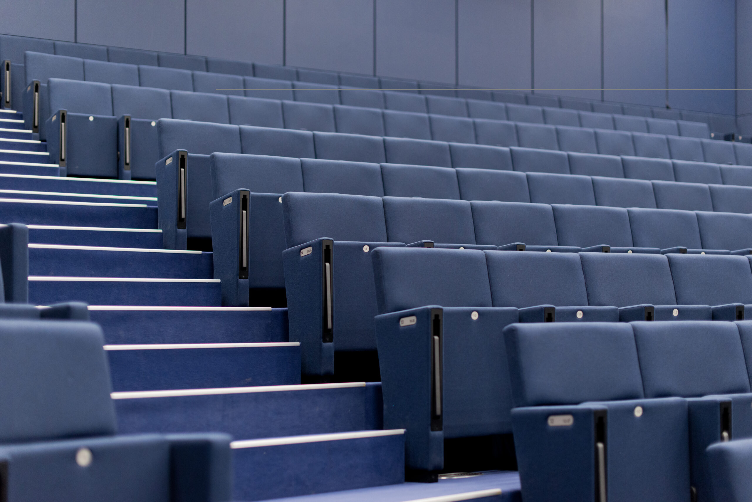 Rangées de chaises pliantes bleues disposées dans une salle de conférence, séparées par un escalier central