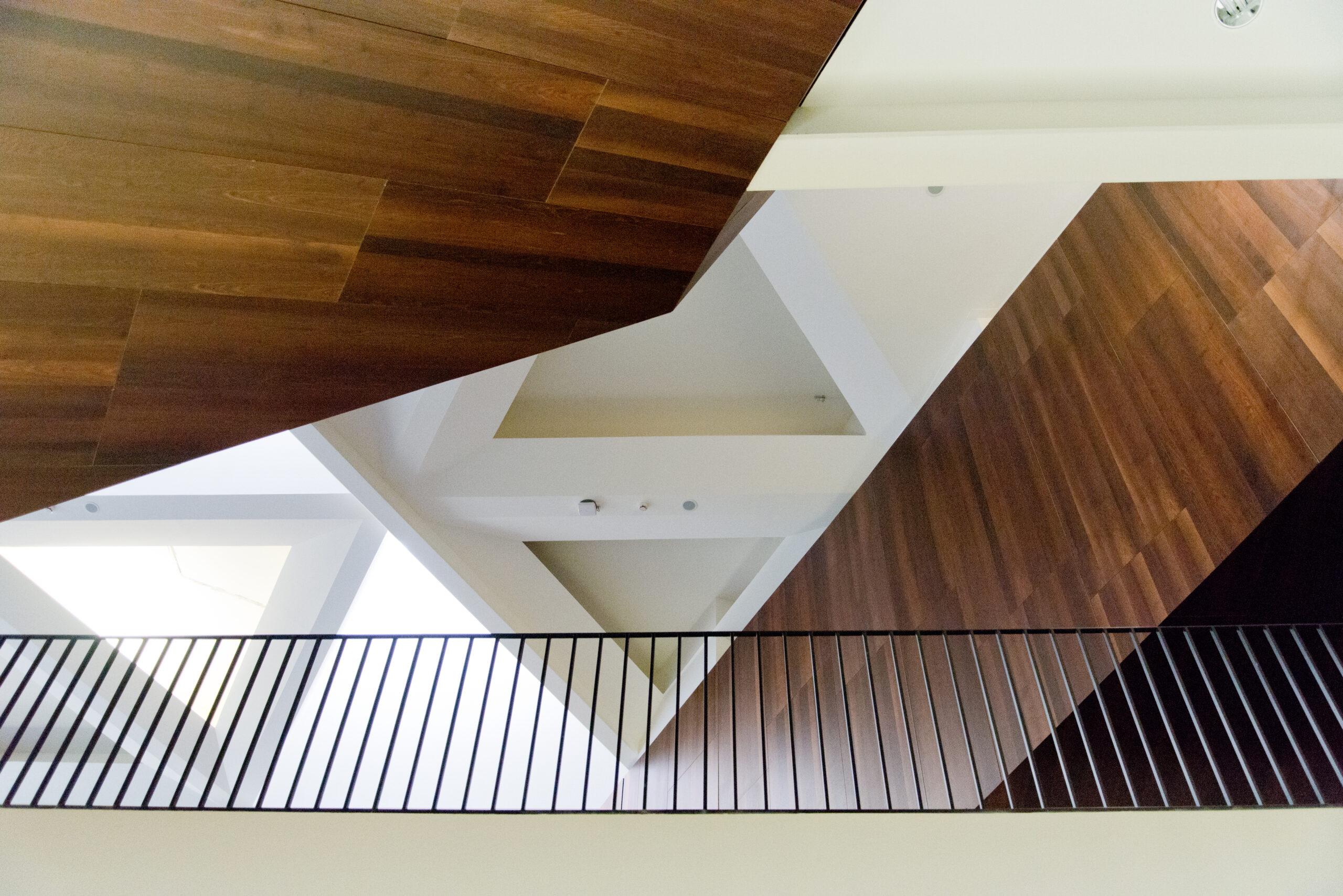 Vue du plafond partiellement habillé de bois et partiellement blanc, avec une rambarde continue au niveau de l’étage supérieur