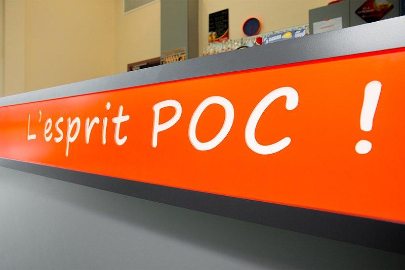 Vue rapprochée du comptoir de bar avec un encart orange affichant l’inscription « l’esprit POC! » — un aménagement de caractère réalisé par Arche du Bois, combinant identité visuelle forte et design contemporain