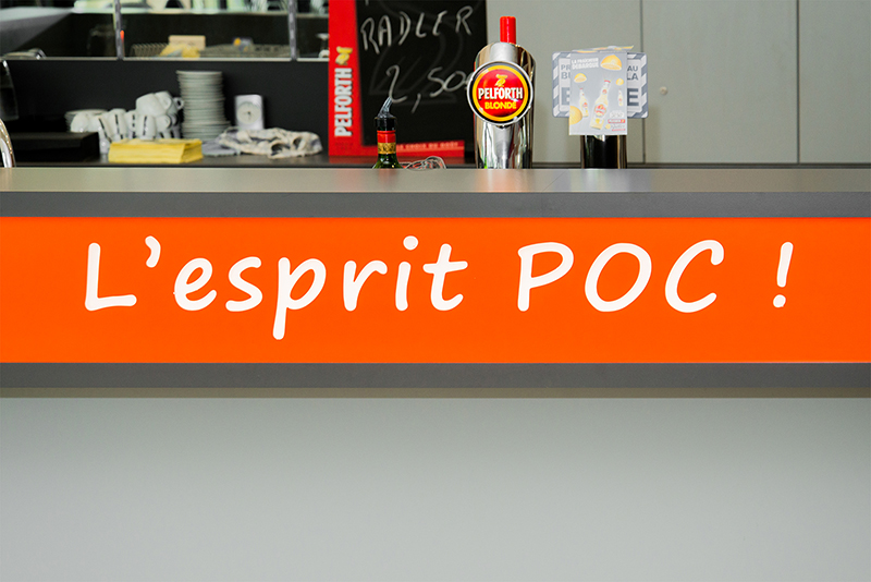 Vue rapprochée du comptoir de bar avec un encart orange affichant l’inscription « l’esprit POC! » — un aménagement de caractère réalisé par Arche du Bois, combinant identité visuelle forte et design contemporain