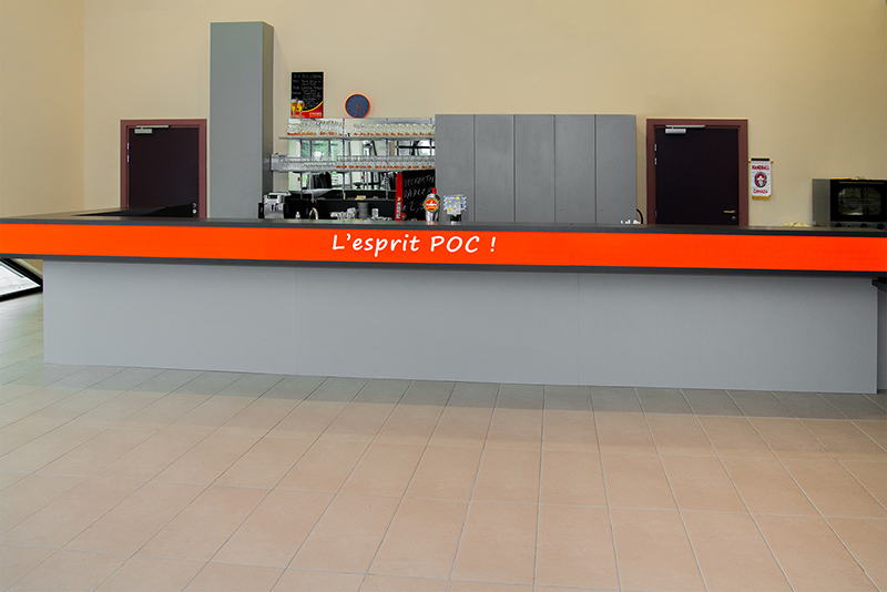 Comptoir de bar gris surmonté d’une bande orange distinctive, avec à l’arrière un placard intégré et une porte