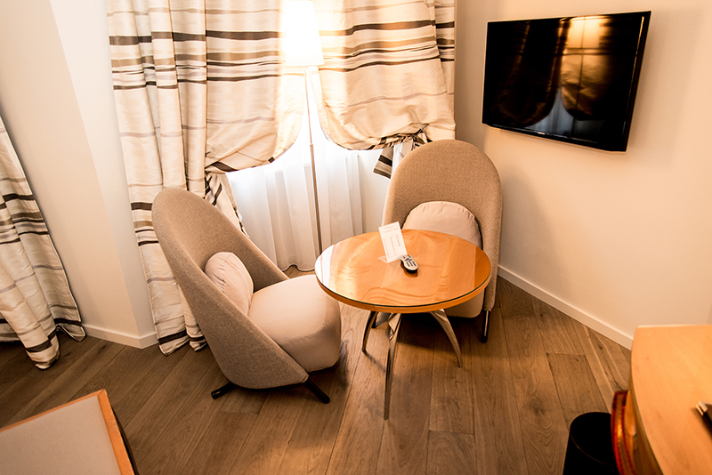 Deux fauteuils confortables accompagnés d’une table basse, avec un rideau en arrière-plan et un téléviseur positionné sur le côté