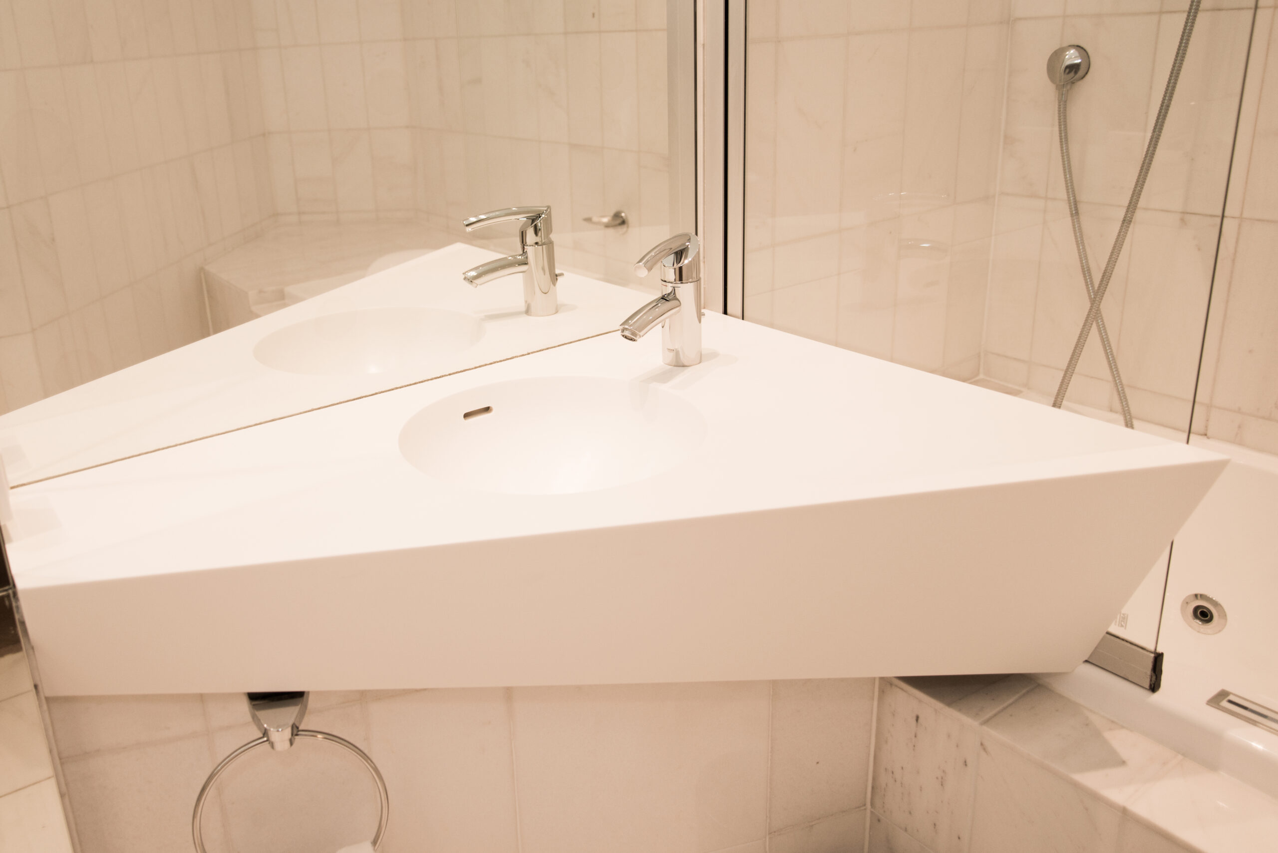 vasque blanc de forme triangulaire avec un miroir mural placé juste derrière, situé à droite d’une cabine de douche — un agencement sanitaire sur mesure signé Arche du Bois, alliant originalité, fonctionnalité et design épuré.