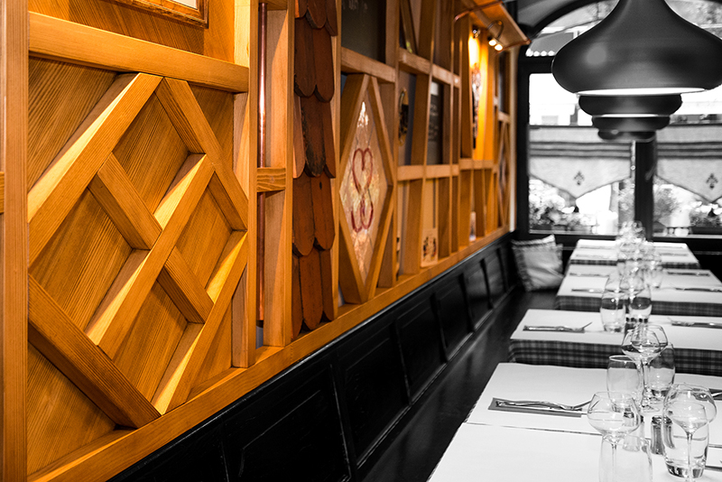 Vue rapprochée d’un mur en bois naturel, avec plusieurs tables visibles sur le côté — un agencement chaleureux et authentique signé Arche du Bois, mettant en valeur les matériaux nobles et l’ambiance conviviale de l’espace.