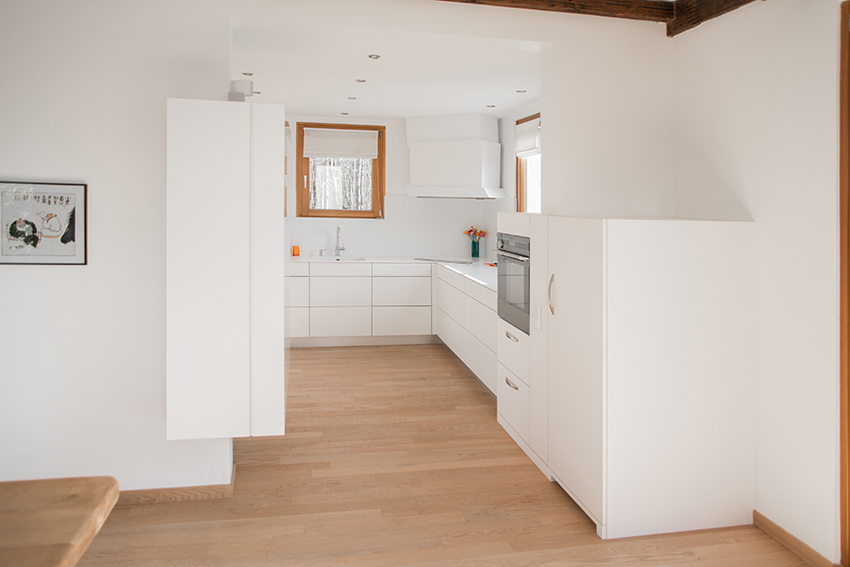 Cuisine au design blanc épuré avec meubles et murs blancs, contrastée par un sol en parquet bois naturel — un agencement sobre et élégant réalisé par Arche du Bois.