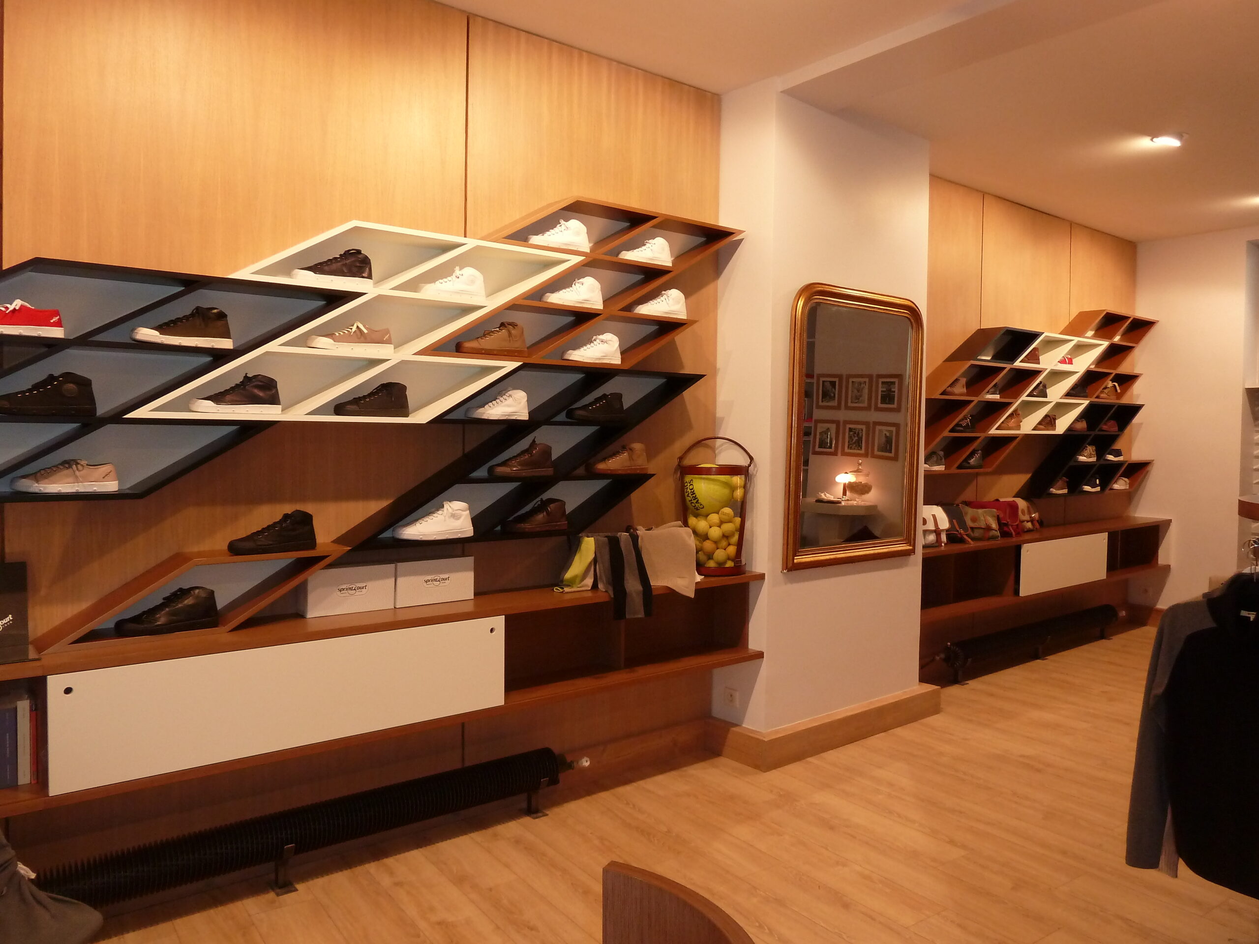 Étagères murales en forme de losange intégrées dans le mur, utilisées pour exposer des chaussures, avec un miroir placé entre deux parois opposées — un agencement créatif et fonctionnel signé Arche du Bois.
