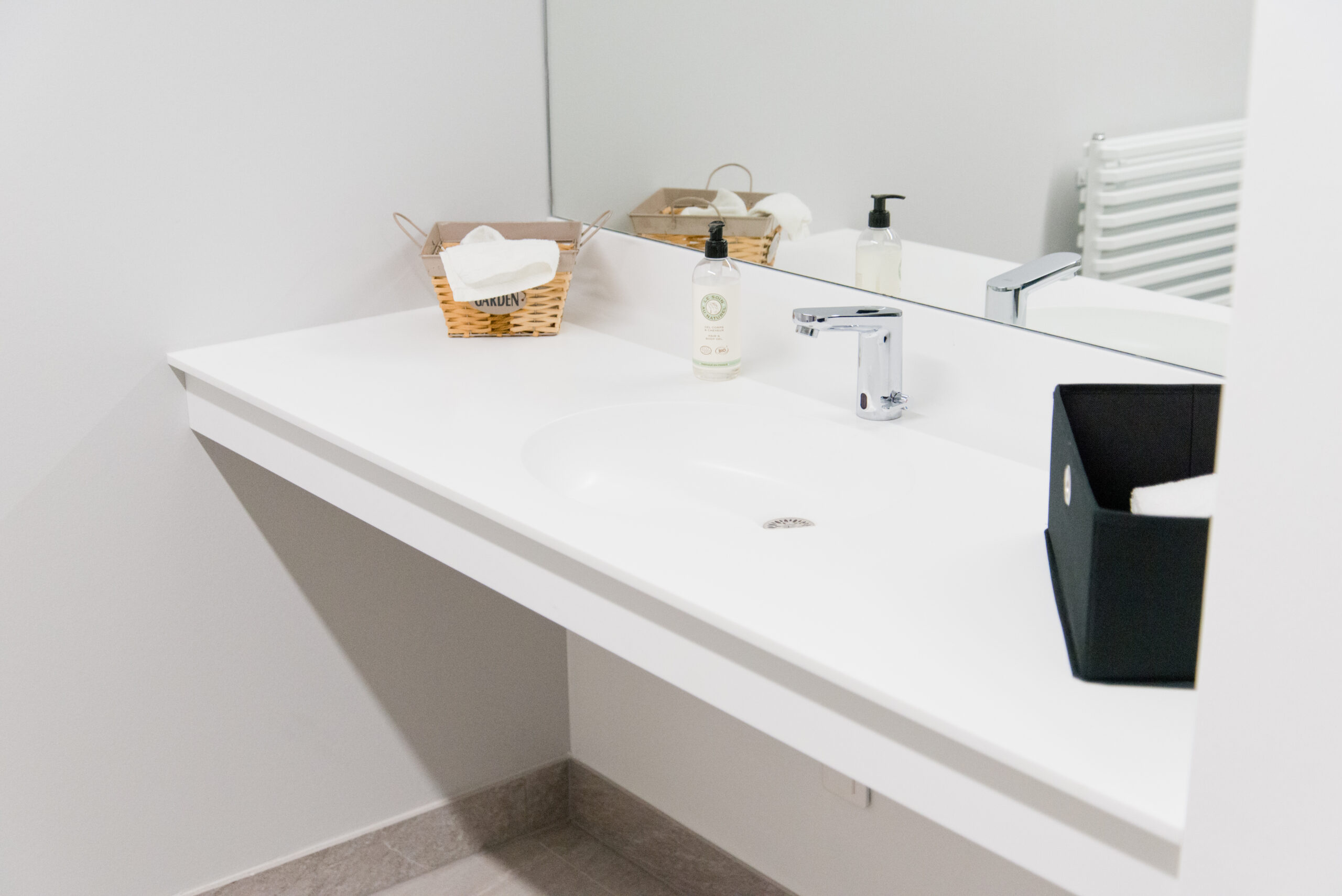 Lavabo blanc avec miroir mural positionné juste au-dessus — un aménagement simple et raffiné signé Arche du Bois, mettant en valeur la fonctionnalité et l’élégance des lignes épurées