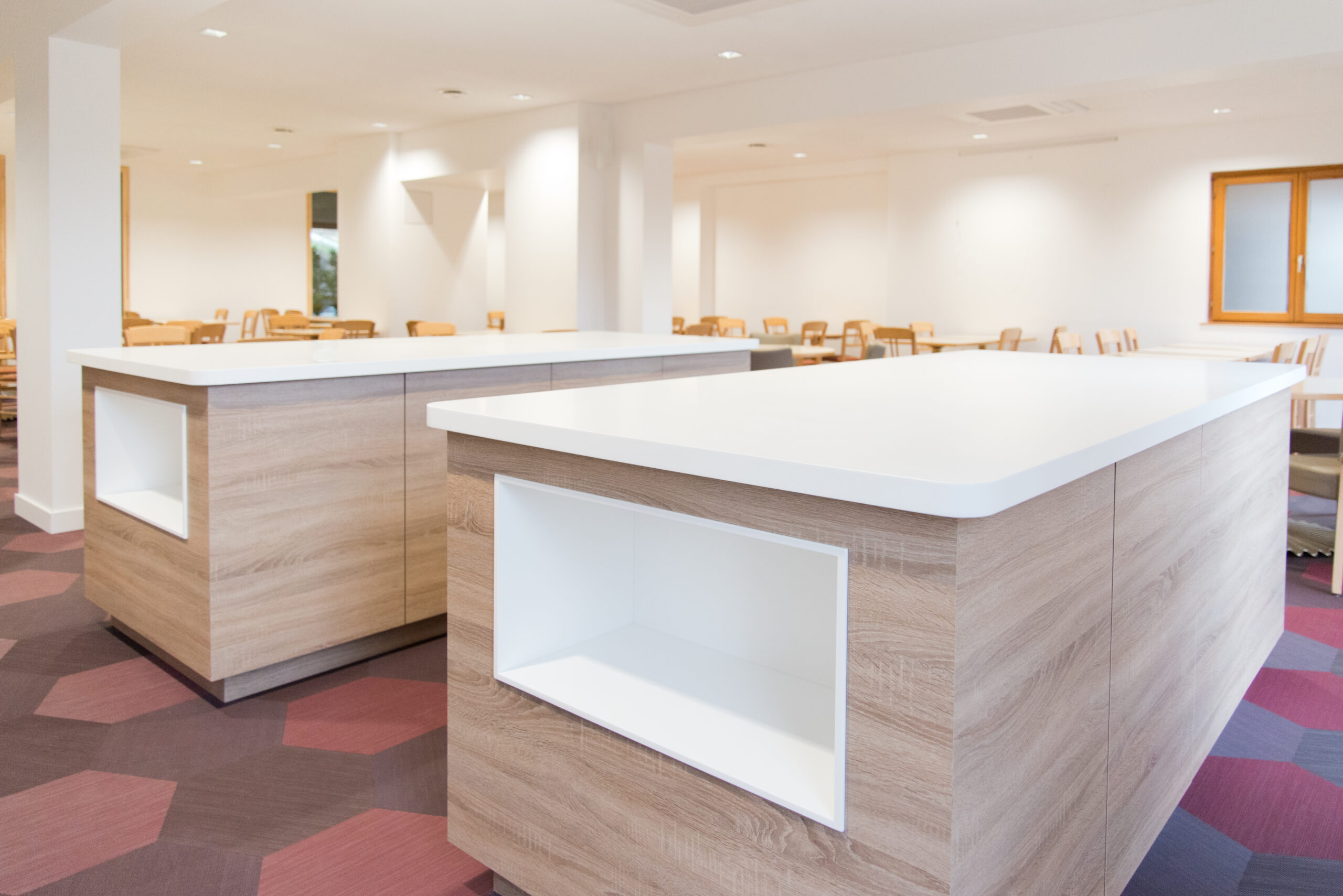 Deux grandes tables en bois avec plateaux blancs, disposées dans un espace ouvert