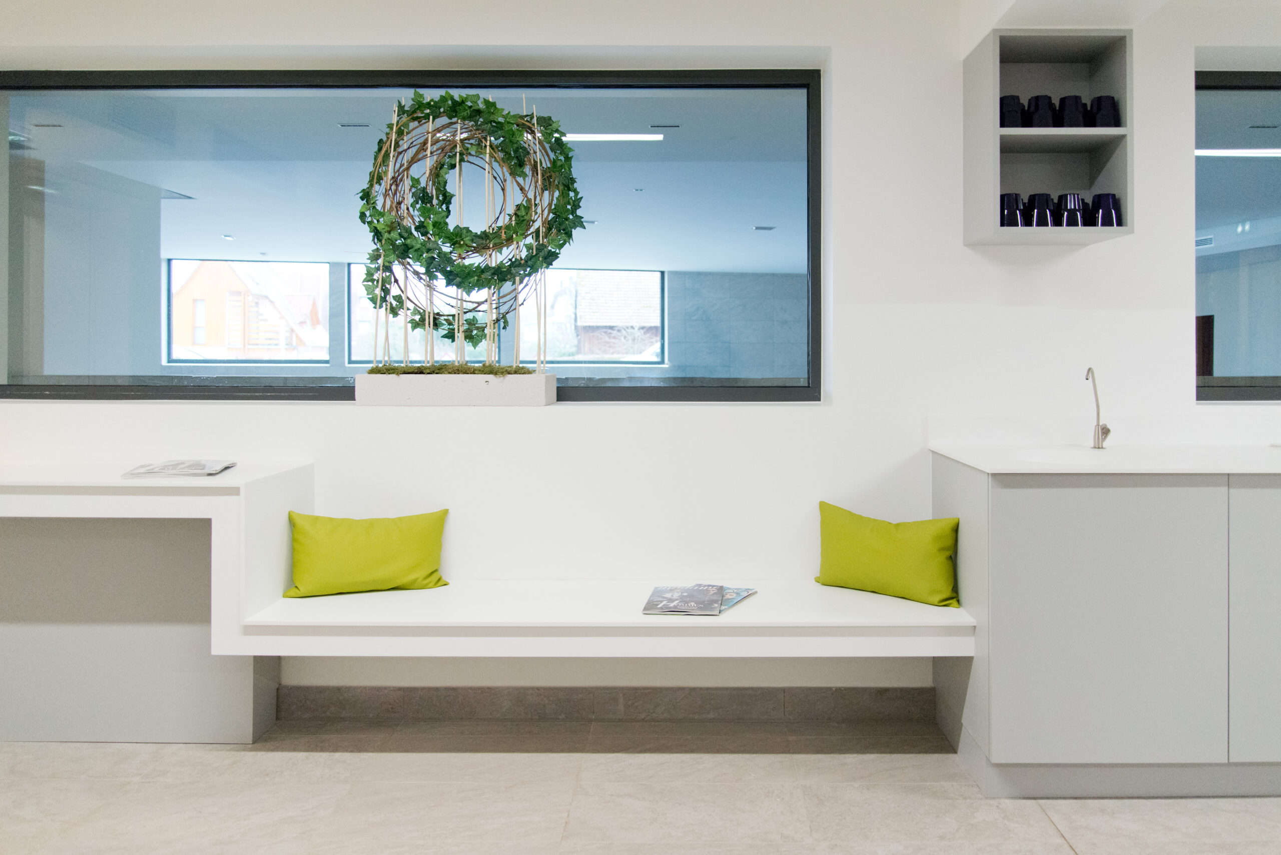 Coin lavabo avec meuble de rangement et assise blanche, situé devant une grande fenêtre vitrée