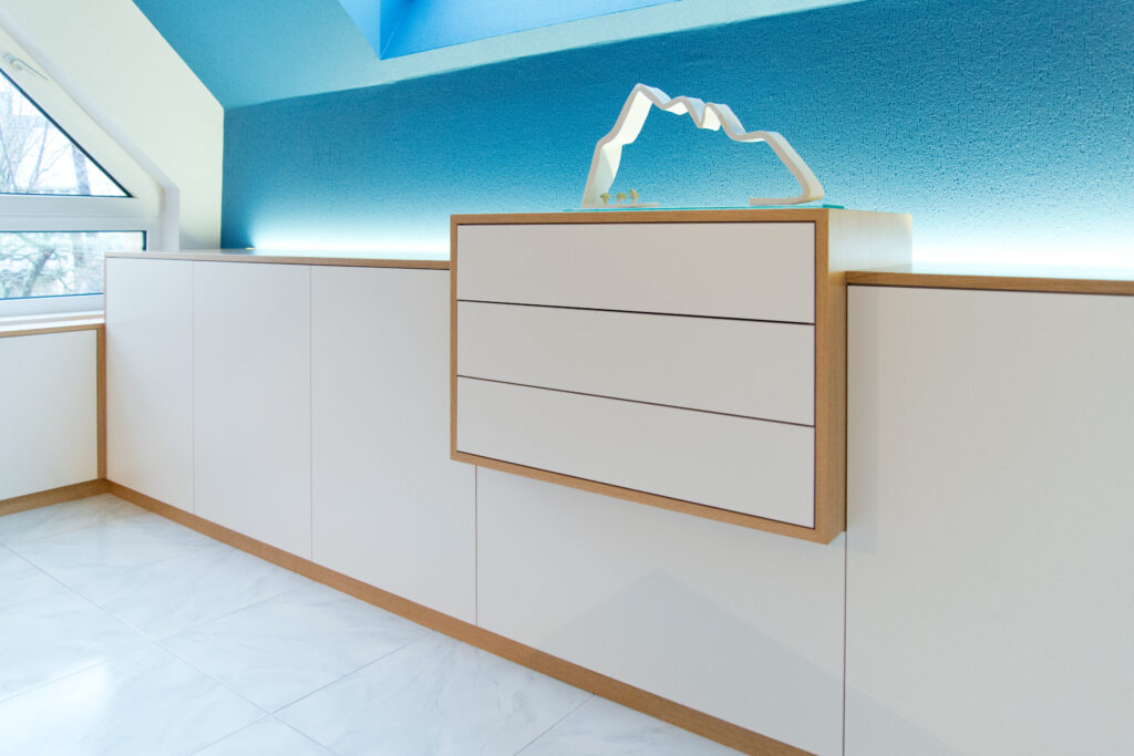 Meuble de rangement blanc encadré de bois naturel, positionné devant un mur bleu, réalisé sur mesure par Arche du Bois.