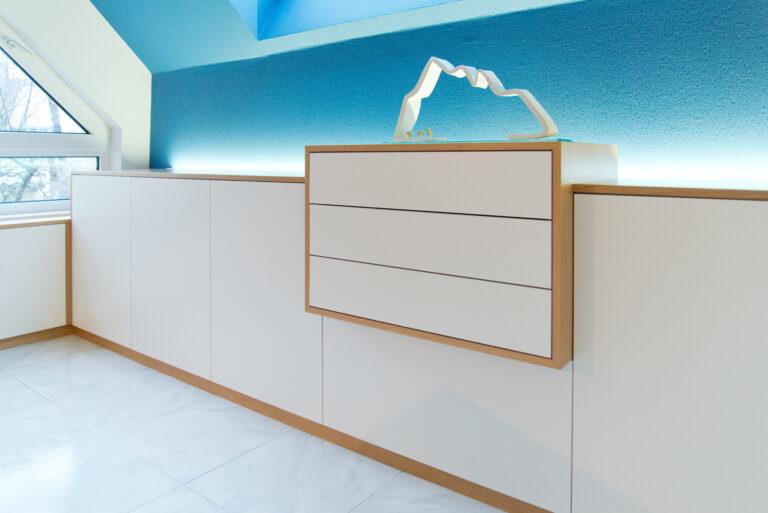 Meuble de rangement blanc encadré de bois naturel, positionné devant un mur bleu, réalisé sur mesure par Arche du Bois. Bureau sur mesure Alsace