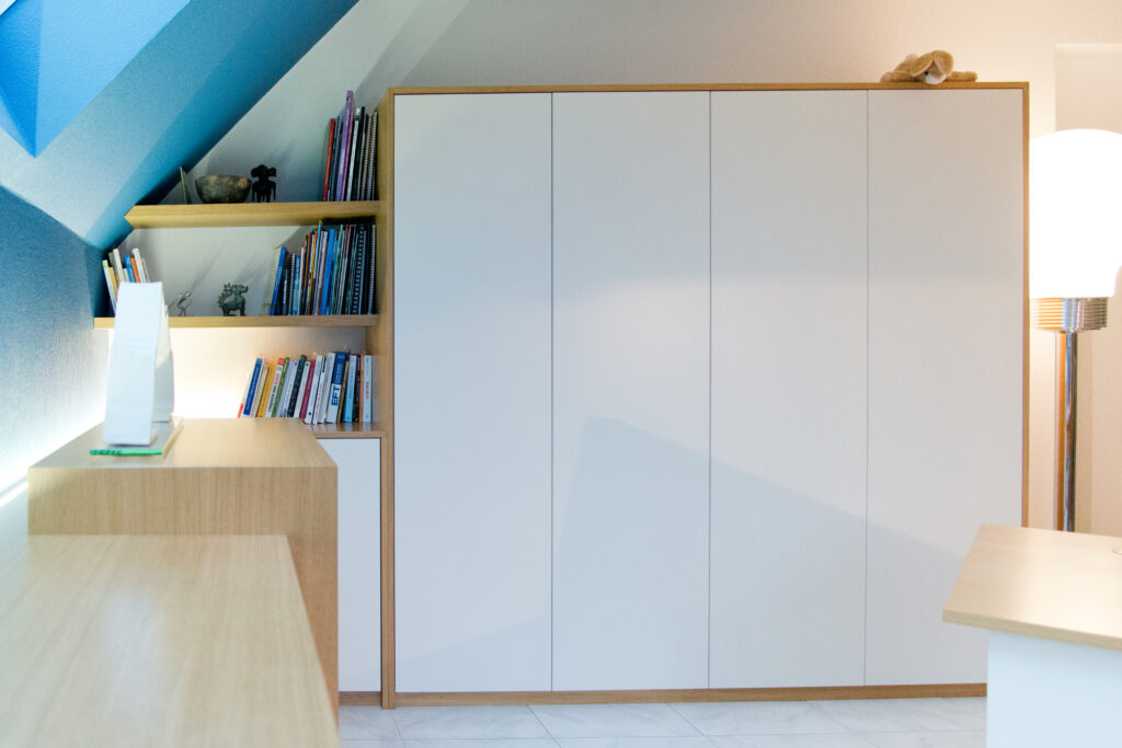 Meuble blanc encadré de bois clair, accompagné d'une petite bibliothèque intégrée sur le côté gauche et d’un abat-jour moderne à droite, agencement sur mesure signé Arche du Bois