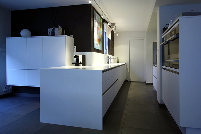 Cuisine sur mesure blanc et noir réalisée par LDC Agencement – L’Arche du Bois : îlot central blanc, placards intégrés à droite avec four et micro-ondes, et rangements muraux à gauche.