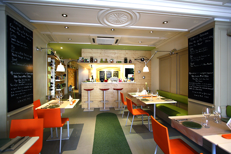 Salle de restaurant avec un comptoir de bar en fond, et des tables accompagnées de chaises disposées de chaque côté de l’espace — un agencement convivial et structuré signé Arche du Bois, pensé pour le confort et la fluidité.