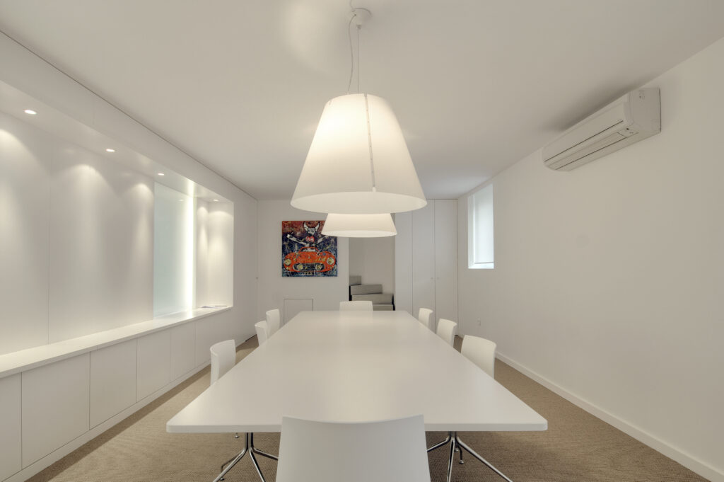Salle de réunion aménagée par Arche du Bois, avec une grande table blanche entourée de chaises design, deux suspensions au-dessus du plateau, et un tableau décoratif accroché au mur en fond de pièce.