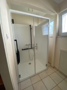 Cabine de douche Danaé by L'Arche du Bois avec double porte vitrée fermée, laissant voir le siège PMR et les barres de maintien à l'intérieur.