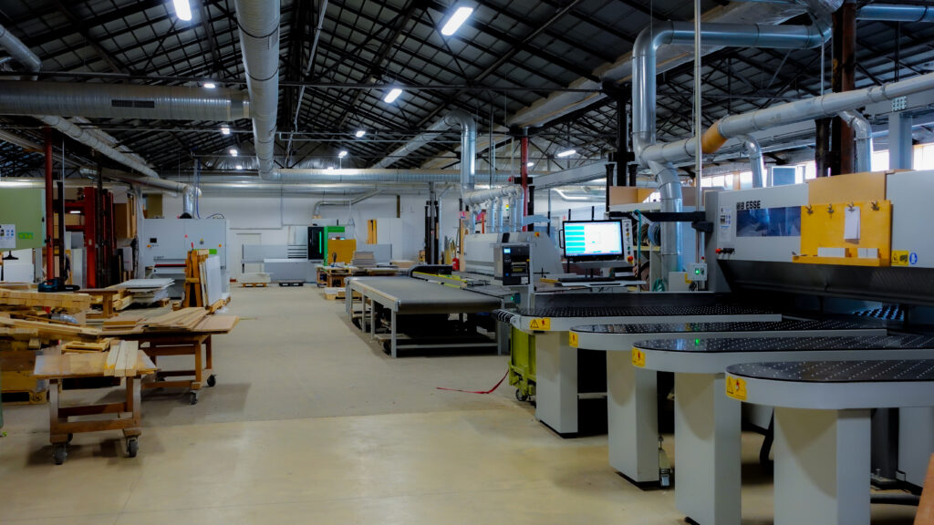 Intérieur de l'atelier de L'Arche du Bois : machines CNC modernes pour le bois massif, zone de production et stock de bois.