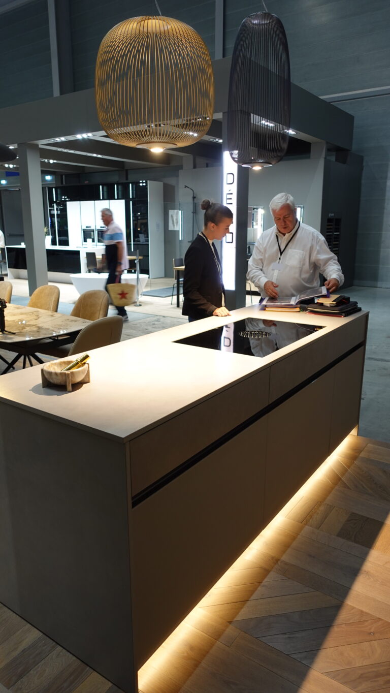 Vue détaillée d'un cabinet de cuisine moderne (plan de travail et façades) intégrant une plaque de cuisson à induction et des éclairages LED sous les meubles hauts. Conception de cuisine par l'Arche du Bois.