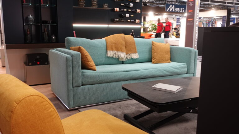 Canapé-dienne bleu convertible en deux lits superposés, avec une table basse devant. À l'arrière, rangement mural intégré pour bouteilles et éclairage d'ambiance. Solution de gain de place de l'Arche du Bois.