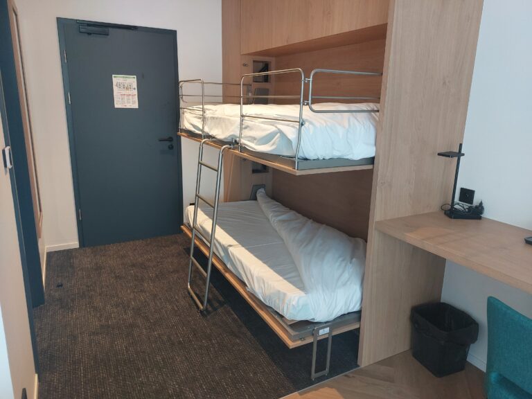 Lits superposés escamotables entièrement déployés avec une échelle métallique centrale et des barrières de sécurité, intégrés dans un habillage en bois clair.