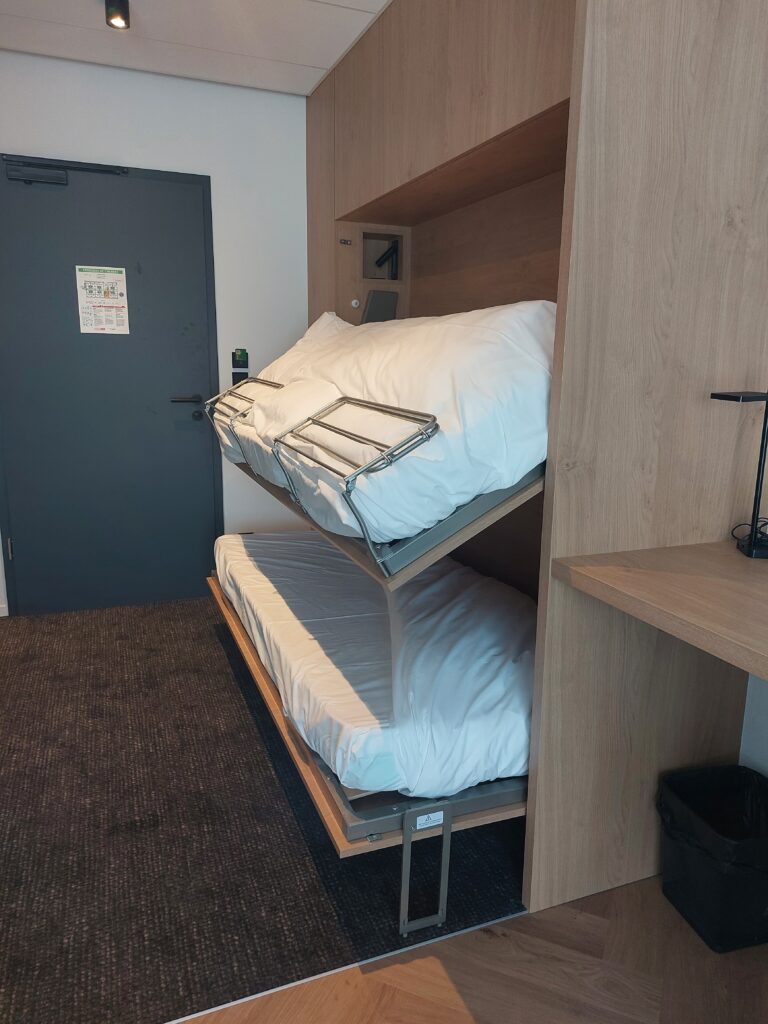 Lit superposé escamotable en bois clair intégré dans un mur de rangement sur mesure, montrant le mécanisme de pliage dans une chambre moderne.