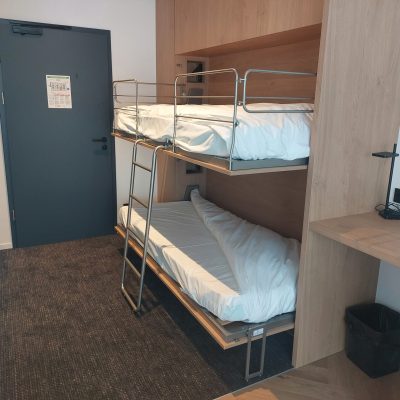 Lits superposés escamotables entièrement déployés avec une échelle métallique centrale et des barrières de sécurité, intégrés dans un habillage en bois clair.