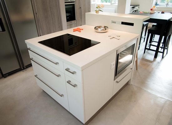 Îlot central blanc équipé de tiroirs et placards intégrés, surmonté d’une plaque de cuisson vitrocéramique noire. Un four encastré complète cet espace fonctionnel au design épuré, idéal pour une cuisine contemporaine