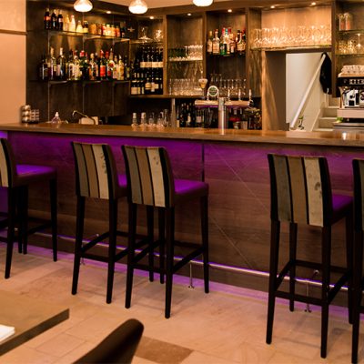 Bar en bois avec plusieurs tabourets alignés à l’arrière, et un éclairage LED intégré sous le comptoir