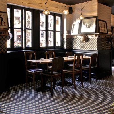 Deux ensembles table et chaises placés face à une fenêtre, dans un espace à l’atmosphère traditionnelle — un agencement authentique signé Arche du Bois, combinant mobilier en bois et charme intemporel.
