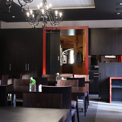 Salle à manger avec plusieurs tables et chaises, donnant sur une entrée visible en fond de pièce — un agencement fluide et convivial réalisé par Arche du Bois, pensé pour le confort et la circulation naturelle des usagers. agencement professionnel​