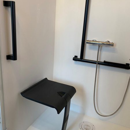Gros plan sur l'intérieur blanc de la douche Danaé by L'Arche du Bois, mettant en évidence le siège PMR rabattable et le système de double barre d'appui (verticale en I et transversale en T).