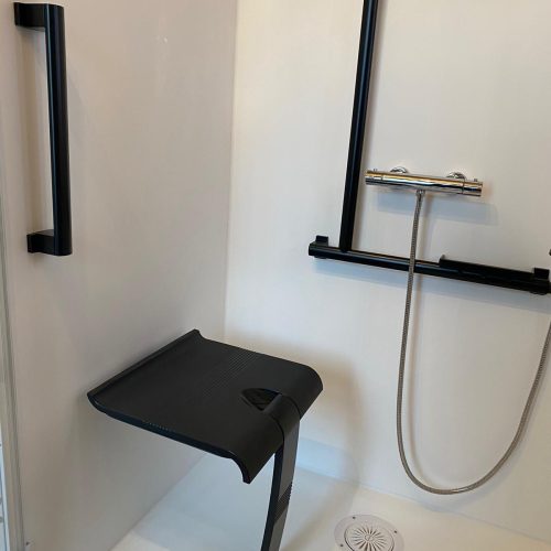 Gros plan sur l'intérieur blanc de la douche Danaé by L'Arche du Bois, mettant en évidence le siège PMR rabattable et le système de double barre d'appui (verticale en I et transversale en T).