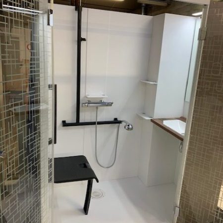 Cabine de douche Danaé by L'Arche du Bois ouverte. Intérieur équipé d'un siège PMR, d'une double barre d'appui (en I et en T) à gauche, et d'un espace vasque avec miroir intégré à droite.