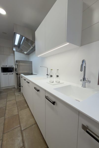 Plan de travail blanc avec éviers intégrés et robinetterie moderne pour une cuisine professionnelle au design minimaliste réalisée pour le projet cuisine Bugatti.